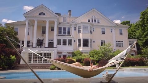 Joe Budden mansion where Cyn Santana is sun basking in front of blue swimming pool and white colored mansion  